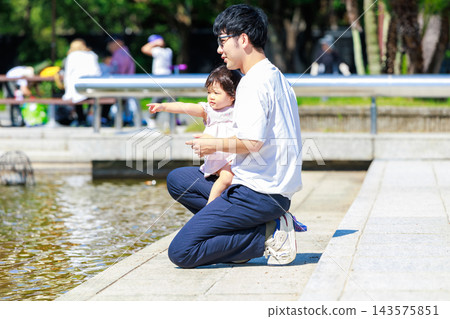 公園裡，父親抱著一個蹣跚學步的孩子。 143575851