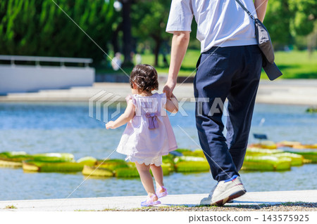 公園裡,一個小女孩牽著爸爸的手。 公園裡,一個小女孩牽著爸爸的手。 143575925