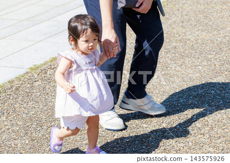 公園裡,一個小女孩牽著爸爸的手。 公園裡,一個小女孩牽著爸爸的手。 143575926