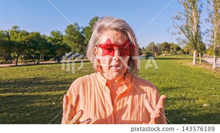 Mature woman wearing star glasses talking outdoors in park Mature woman wearing star glasses talking outdoors in park 143576189