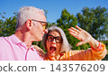 Senior couple sharing a joyful outdoor selfie moment 143576209