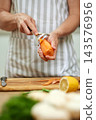 Hands peeling an orange carrot over a wooden cutting board with a vegetable peeler. Preparing fresh produce for cooking 143576956