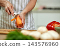 Hands of a woman chef peeling a fresh organic carrot over a wooden cutting board in a kitchen preparing a healthy meal 143576960