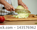 Hands cutting green cabbage with a sharp knife on a wooden cutting board, making a healthy vegetable salad 143576962