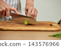 Chef hands preparing food, cutting fresh cucumber with a knife on a wooden chopping board in a modern kitchen 143576966