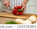 Hands slicing a fresh red bell pepper with a knife on a wooden cutting board, preparing healthy food in the kitchen 143576969