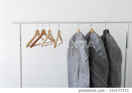 Garment storage bags protect seasonal clothes on rack with wooden hangers. Fabric care dry cleaning dust protection closet organization. Seasonal wardrobe change smart housekeeping. 143577531