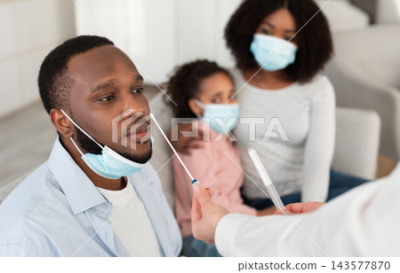 Medical worker doctor taking corona virus sample from potentially infected African American man, inserting a long swab inside nose, people wearing protective medical masks Medical worker doctor taking corona virus sample from potentially infected African American man, inserting a long swab inside nose, people wearing protective medical masks 143577870