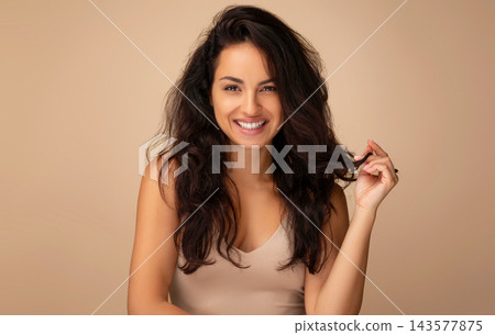 Hair styling, hair care concept. Gorgeous eastern millennial woman in beige top posing on studio background, showing her beautiful long hair after salon hair treatment and smiling at camera Hair styling, hair care concept. Gorgeous eastern millennial woman in beige top posing on studio background, showing her beautiful long hair after salon hair treatment and smiling at camera 143577875