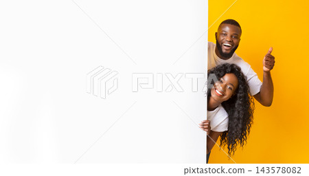 African American woman And Guy Holding White Advertising Board, guy showing thumb up, yellow studio background, panorama African American woman And Guy Holding White Advertising Board, guy showing thumb up, yellow studio background, panorama 143578082