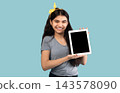 Cute Indian adolescent girl holding tablet pc with blank screen on blue studio background, space for app or website design. Smiling teenager showing touch pad with mockup for your ad 143578090