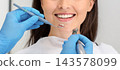 Beautiful smile concept. Smiling young woman attending dental clinic, hands of dentist with drilling tools, cropped 143578099