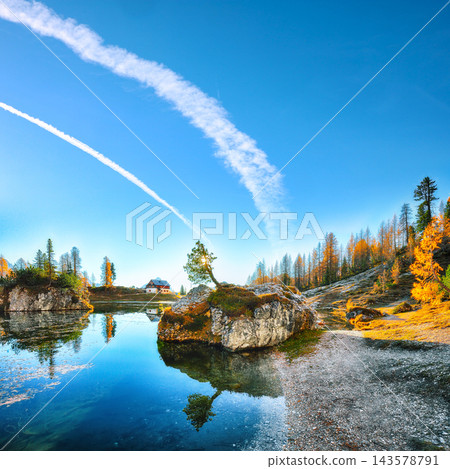 Amazing autumn view of  Lake Federa  at sunrise with majestic rocky mount and colorful trees glowing sunlight in Dolomites 143578791