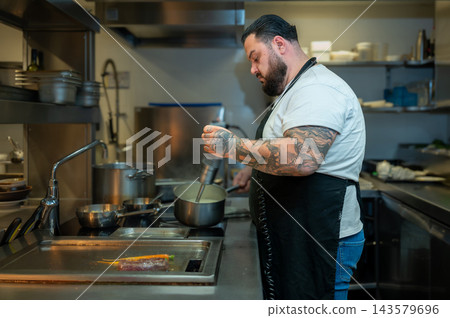 Focused Chef Preparing Dish. Handsome chef concentrating on cooking a dish in a professional restaurant kitchen. Focused Chef Preparing Dish. Handsome chef concentrating on cooking a dish in a professional restaurant kitchen. 143579696