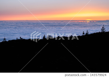 Warm sunset light spreads across a sea of clouds below the ridge in Teide National Park. Perspective and calm for wellbeing travel and mental reset campaigns. Warm sunset light spreads across a sea of clouds below the ridge in Teide National Park. Perspective and calm for wellbeing travel and mental reset campaigns. 143579924