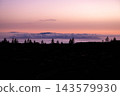 Pink dusk over an ocean of cloud and pine silhouettes. Pink and violet dusk spreads over an ocean of cloud with pine silhouettes on the ridge in Teide National Park. Calm and distance for wellbeing 143579930