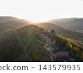 Backlit fortress glowing in sunset light. Castle Haut-Koenigsbourg, Alsace, France - April 10, 2026 - Backlit fortress glowing in sunset light, amber rim highlights towers, long access road visible 143579935