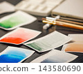 Closeup color palette chart papers on wooden studio desk. Watercolor paint samples and brushes on workspace Colorful color palette chart shows pigment gradient wash samples Artistic watercolor palette 143580690