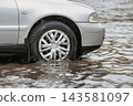 A car is navigating through flooded city streets during a downpour. Water creates puddles around the vehicle as rain continues to fall 143581097