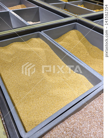 Millet grains displayed in gray supermarket bins present a traditional cereal food with a bright yellow color, dry texture and valuable nutritional properties Millet grains displayed in gray supermarket bins present a traditional cereal food with a bright yellow color, dry texture and valuable nutritional properties 143582354