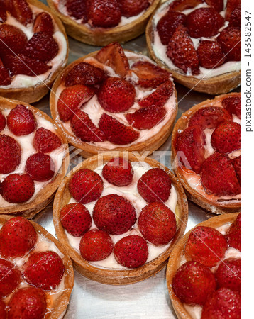 Tartlets topped with fresh red strawberries create a colorful dessert presentation, combining a delicate pastry base with an attractive fruit decoration 143582547