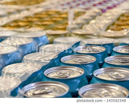 Blue and yellow cans filled with carbonated beverages are stored in packaging at a warehouse, presenting packaged drinks organized as part of a beverage supply 143582548
