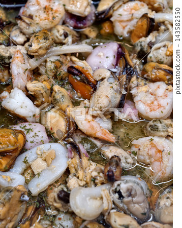 Mixed seafood cocktail with mussels, shrimp, mollusks and crustaceans immersed in seasoned oil and arranged on a supermarket seafood counter Mixed seafood cocktail with mussels, shrimp, mollusks and crustaceans immersed in seasoned oil and arranged on a supermarket seafood counter 143582550