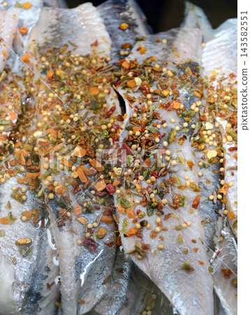 Herring fillet with spices in oil displayed on a supermarket seafood counter, offering prepared fish from the refrigerated fish department for customer selection Herring fillet with spices in oil displayed on a supermarket seafood counter, offering prepared fish from the refrigerated fish department for customer selection 143582551