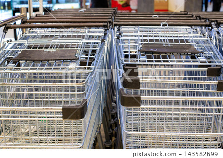 Rows of empty metal shopping trolleys under a canopy at the supermarket entrance. Neatly arranged metal shopping carts inside the supermarket. Overhead view. Rows of empty metal shopping trolleys under a canopy at the supermarket entrance. Neatly arranged metal shopping carts inside the supermarket. Overhead view. 143582699