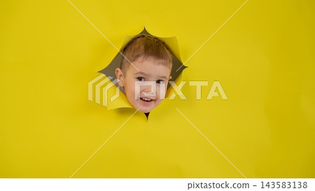 A mischievous boy peeks out through a hole in a yellow cardboard background. A mischievous boy peeks out through a hole in a yellow cardboard background. 143583138