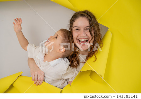 Caucasian little boy and his mother tearing yellow paper background. Caucasian little boy and his mother tearing yellow paper background. 143583141