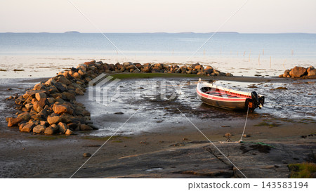Small motorboat moored on a muddy tidal flat at low tide. Vessel secured near a stone breakwater on the rocky coast at White Sea, Russia. Nautical marine landscape Small motorboat moored on a muddy tidal flat at low tide. Vessel secured near a stone breakwater on the rocky coast at White Sea, Russia. Nautical marine landscape 143583194
