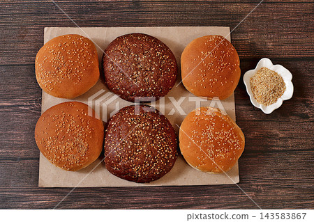 Fluffy buns for burgers, cheeseburgers, and sandwiches. Freshly baked, golden brown sesame seed buns on craft paper atop a kitchen counter,advertisement for cafe or bakery or fastfood restaurant menu. Fluffy buns for burgers, cheeseburgers, and sandwiches. Freshly baked, golden brown sesame seed buns on craft paper atop a kitchen counter,advertisement for cafe or bakery or fastfood restaurant menu. 143583867