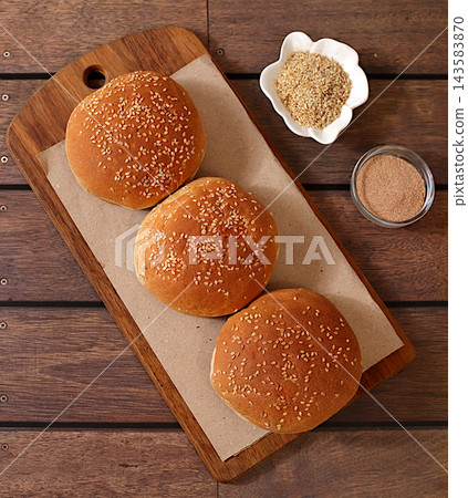 Golden brown, freshly baked sesame seed buns on artisanal food grade on a wooden tray a kitchen counter, fluffy buns for burgers, cheeseburgers and sandwiches. Advertisement for a cafe or bakery, Golden brown, freshly baked sesame seed buns on artisanal food grade on a wooden tray a kitchen counter, fluffy buns for burgers, cheeseburgers and sandwiches. Advertisement for a cafe or bakery, 143583870