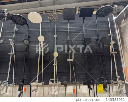 Shower systems line showroom display, with varied overhead rain heads and handheld sprayers mounted against dark perforated panels. Fixtures present finishes and designs for home bathroom renovation. Shower systems line showroom display, with varied overhead rain heads and handheld sprayers mounted against dark perforated panels. Fixtures present finishes and designs for home bathroom renovation. 143583931