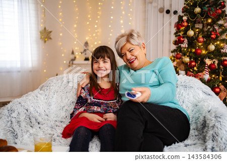 Grandmother and granddaughter watching TV together during Christmas holiday Grandmother and granddaughter watching TV together during Christmas holiday 143584306
