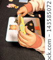 A child's small hands pick up and apply magnetic clothing elements to a picture of a girl on a board 143585072