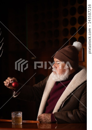 Elegant Santa examining red Christmas ornament at bar Elegant Santa examining red Christmas ornament at bar 143587216