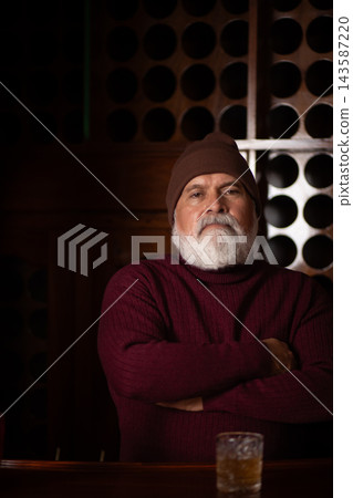Serious senior man in red sweater at elegant bar Serious senior man in red sweater at elegant bar 143587220