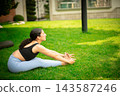 Woman practicing yoga paschimottanasana pose outdoors in garden 143587246