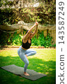 Woman practicing yoga tree pose outdoors on a mat 143587249