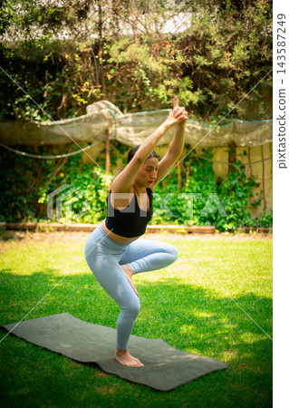 Woman practicing yoga tree pose outdoors on a mat Woman practicing yoga tree pose outdoors on a mat 143587249