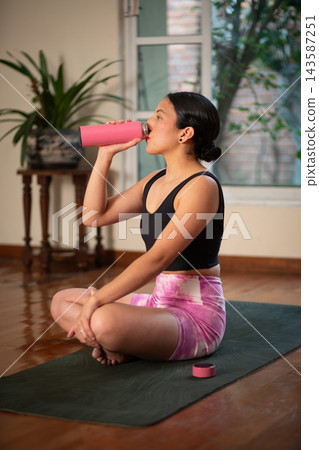 Woman drinking water from bottle after yoga workout at home Woman drinking water from bottle after yoga workout at home 143587251