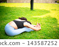 Woman practicing yoga seated forward fold on grass 143587252