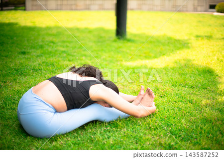 Woman practicing yoga seated forward fold on grass Woman practicing yoga seated forward fold on grass 143587252
