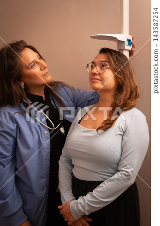 Doctor checking standing patient's height in clinic Doctor checking standing patient's height in clinic 143587254