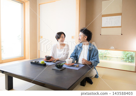 一張日本夫婦享受旅行或國內遊玩的照片，他們坐在類似溫泉旅館的日式房間裡，邊走邊聊。 143588403