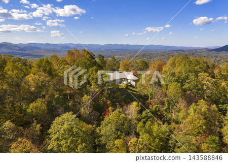Residential homes overlooking colorful forested hills during peak fall season. Peaceful mountain landscape filled with brilliant autumn foliage. 143588846