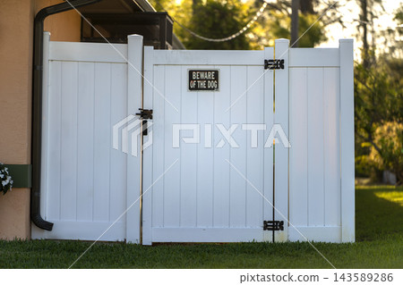 White plastic backyard fence displaying Beware of Dog notice, symbolizing residential safety, private property boundaries, security awareness and suburban living. White plastic backyard fence displaying Beware of Dog notice, symbolizing residential safety, private property boundaries, security awareness and suburban living. 143589286