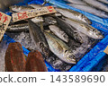 魚店裡，新鮮的竹莢魚整齊地擺放在冰上，旁邊貼著手寫的價格標籤。 143589690